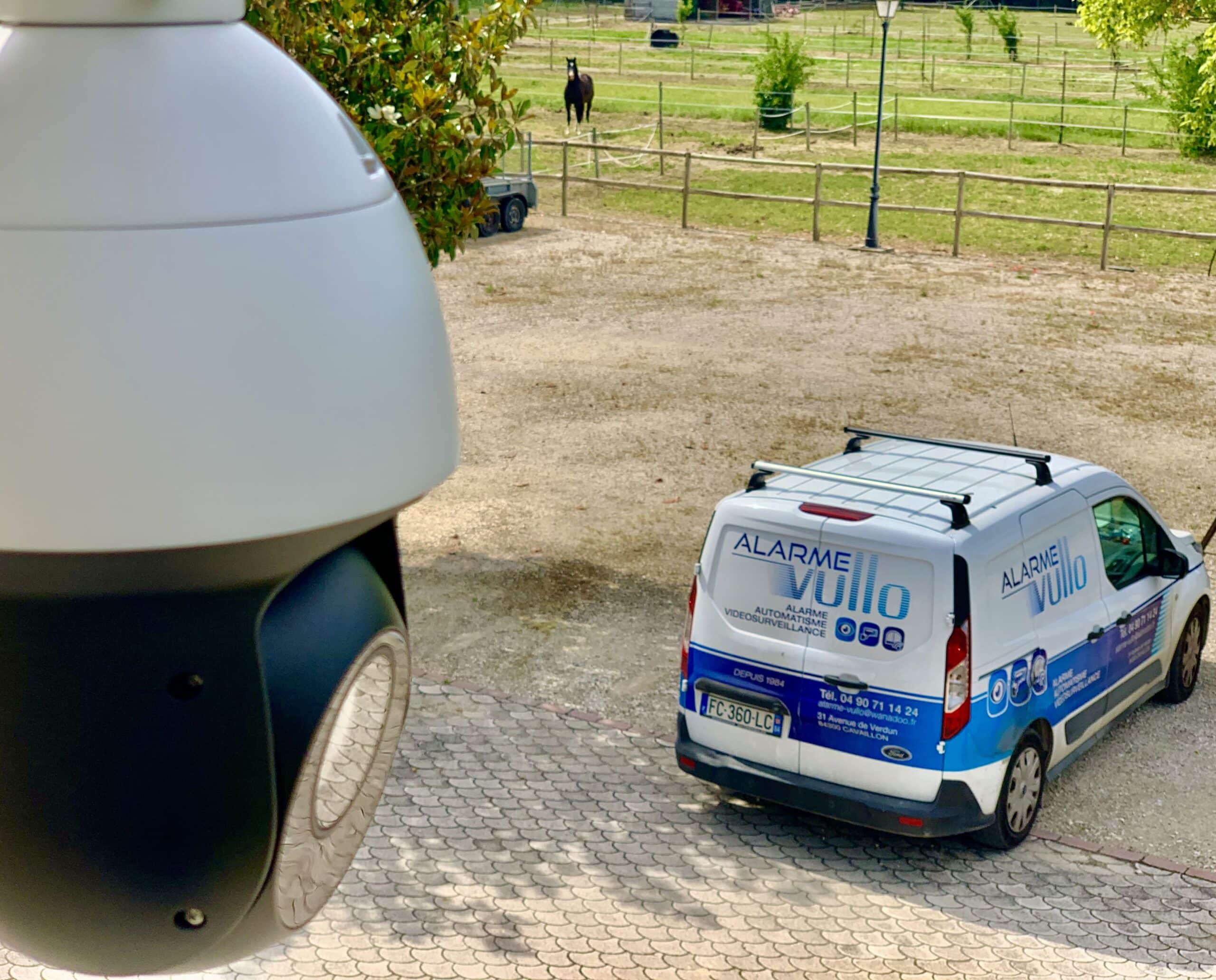 Camera-de-Securite-Vullo-Vehicule-Alarme Caméra de sécurité avec vue de la voiture d'alarme Vullo en arrière-plan, une combinaison de surveillance vidéo et de patrouilles mobiles pour une sécurité accrue.